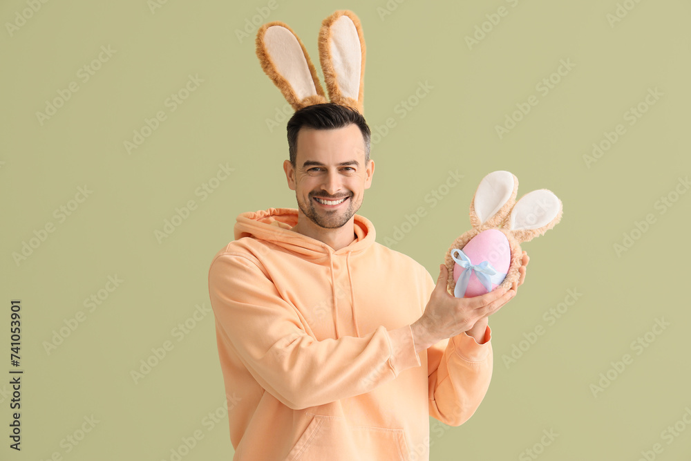 Poster young man with bunny ears and easter egg on green background