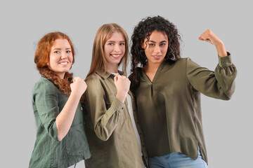Beautiful young happy women showing muscles on grey background. Women history month
