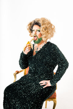 Glamorous Drag Queen in Sparkling Black Attire Enjoys a Banana Seated on a Vintage Chair
