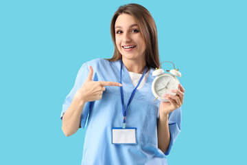 Female doctor pointing at alarm clock on blue background