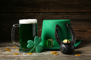 Glass of green beer with clover leaves, Leprechaun's hat, horseshoe and pot full of coins on wooden...