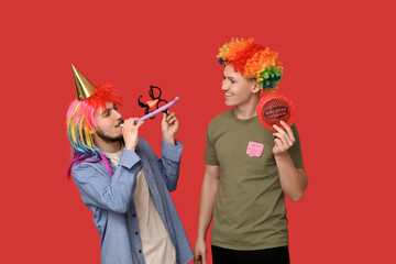 Young friends in funny disguise with whistle and whoopee cushion on red background. April fool's...