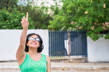 Happy young latina woman with solar eclipse glasses, watching a solar eclipse - obrazy, fototapety, plakaty