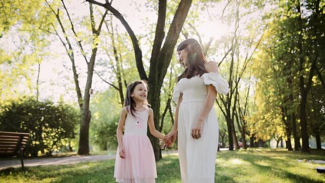 Mom, daughter are walking in park, weekend. Mother holding her daughter's hand in park. Happy family concept