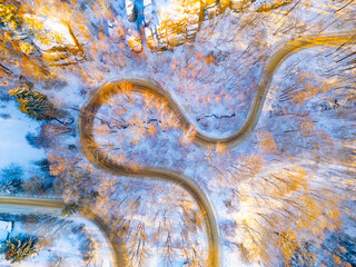 Winding asphalt road in sunny winter morning. Cold and freezy forested countryside.. Aerial view from drone.