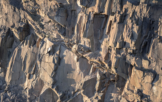 Crumbling rock cliff wall texture with cuts and shadows of The granite rock. View of Spectacular vertical walls cliffs of Salisbury Crags, Nature stone background, Space for text, Selective focus.