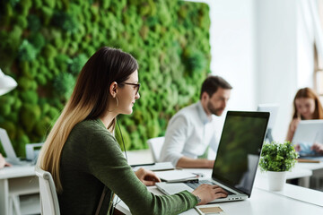young woman is working at laptop in modern office with a living green vertical wall of moss,concept of sustainable development, caring for planet, climate change, increasing oxygen levels, air quality