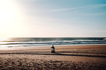 Fototapeta na wymiar Chico parado en mitad de la playa con su moto de campo al atardecer