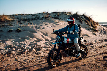 Chico moreno con moto tipo scrambler en la playa viajando 