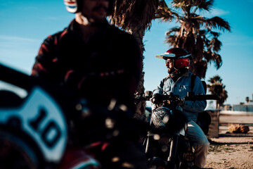 Chico moreno con moto tipo scrambler en la playa viajando 