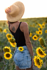 Young woman on her back in a sunflower plantation during golden hour