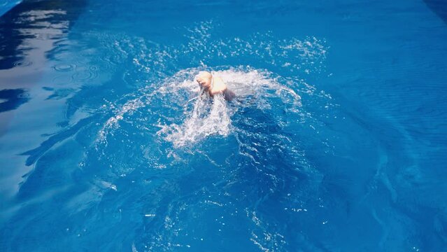 Elegant woman dives into infinity pool at a luxe tropical villa, swims underwater, enjoys serene aquatic escape. Clear blue water embraces solo traveler in exclusive leisure moment. Slow motion.