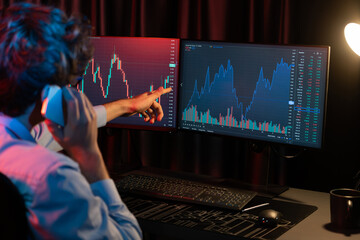 Young investor stock trader calling with broker to invest earning highest profit on current market graph online in real time at neon light modern office, monitor showing investment exchange. Gusher.