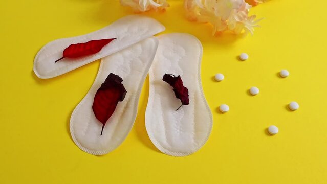 Three feminine pads, three red leaves and pills on yellow.
