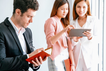 Happy young handsome businessman reading book and working in office with colleagues and friend at...