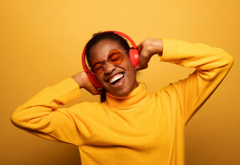 afro american female with dances in rhythm of melody, listens loud song in headphones, holds...