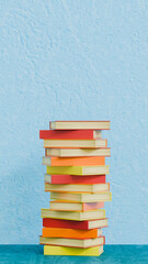 Column of fifteen disordered books of red, yellow and orange colors on blue stage, studies theme