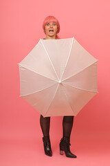 A woman on a pink background hiding behind a white umbrella with an expression on her face as if she was caught off guard.