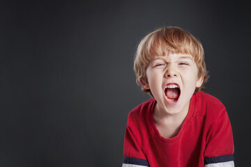 Young angry boy yelling on a gray background