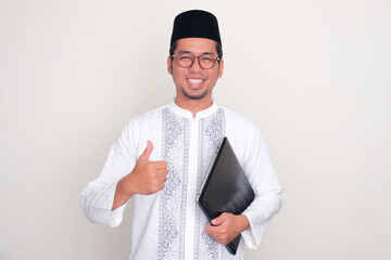 Moslem Asian man smiling and give thumb up while holding a laptop