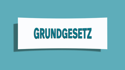 Grundgesetz. Eine weisse Karte mit blaugruener Schrift und Schatten, isoliert auf blaugruenem Hintergrund.