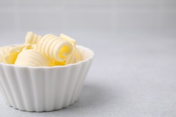 Tasty butter curls in bowl on light grey table, closeup. Space for text