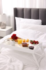 Tray with delicious breakfast on bed in room