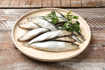 Fresh raw sprats and parsley on wooden table, closeup