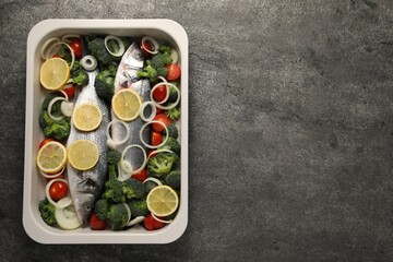 Obraz na płótnie Canvas Raw fish with vegetables and lemon in baking dish on grey textured table, top view. Space for text