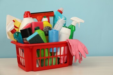 Different cleaning products in plastic basket on wooden table against light blue background