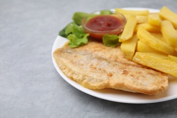 Delicious fish and chips with ketchup and lettuce on gray table, closeup. Space for text