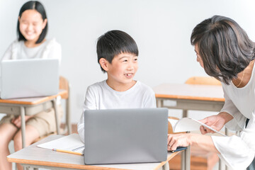 学校の教室でノートパソコンを使いながら勉強する男子小学生と女性講師（教育・先生・授業・家庭教師）
