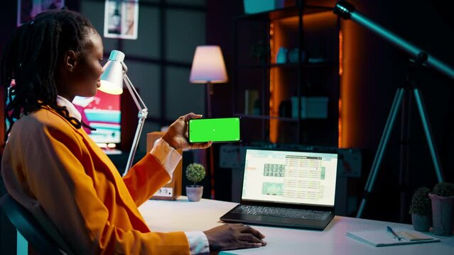 Business student looks at greenscreen on phone app and learning to use tax service software, money management. Young woman holding device with isolated mockup display, e learning. Camera B.