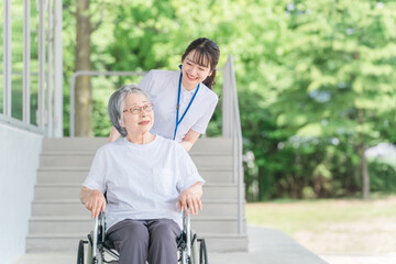 公園を散歩する車椅子に乗った高齢者と介護士（ヘルパー）
