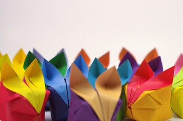Side view of a large crowd of colorful origami rabbits, facing forwards, against a white backdrop....