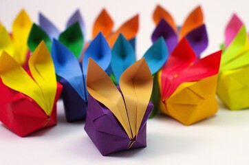 Angled view of a large crowd of colorful origami rabbits, facing forwards, against a white backdrop.