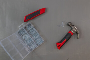 Red and black hammer and box cutter with nails on gray background with copy space in center