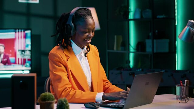 African american girl jamming on music and writing reports for her final bachelor essay, having fun with songs on headset. Student preparing for exams with class notes and materials. Camera A.