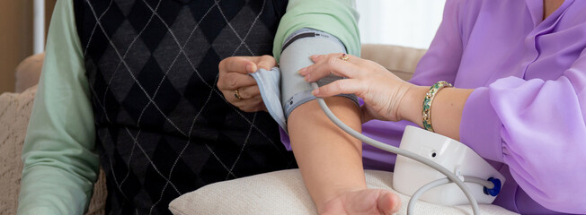 Closeup hands asian senior couple sitting on sofa checking blood pressure with pressure gauge in living room at home, elderly man and woman checkup health and pressure, medical of patient.