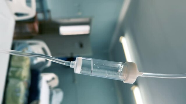 Drip chamber in an IV hanging on a medical infusion stand against the background of blurred medical beds in a clinic ward. Intravenous injections, medical care in a hospital. Vertical video