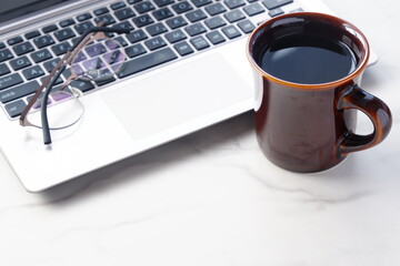 コーヒーを飲みながらノートパソコンでデスクワーク中のイメージ	

