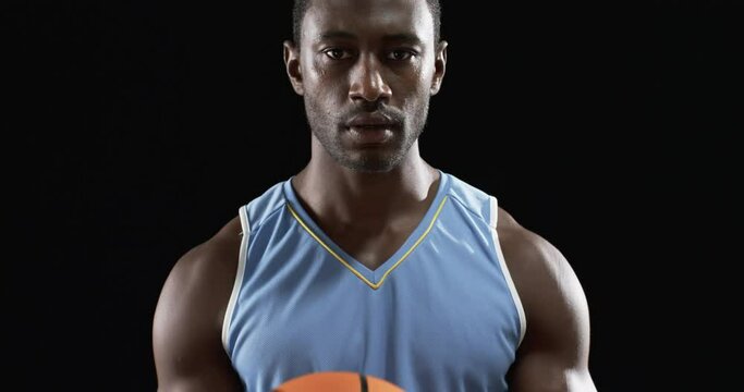 Focused African American athlete holding a basketball on black background