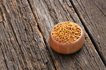 Dried organic fenugreek seeds in the wooden bowl - Trigonella foenum - graecum