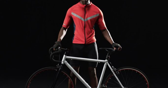 African American cyclist stands with his road bike on a black background