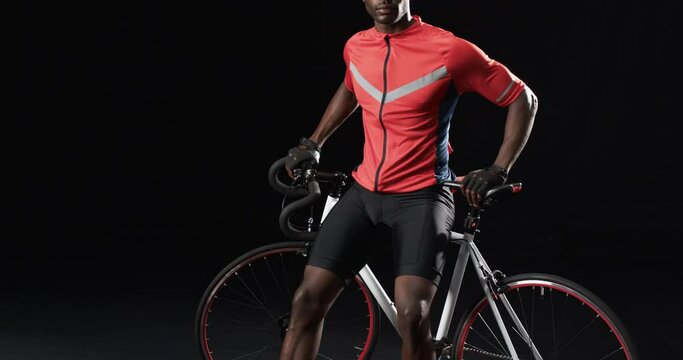 African American cyclist poses confidently on a bicycle on a black background, with copy space