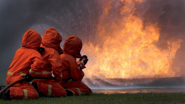Firefighter Rescue team training in fire fighting extinguisher. Teamwork Firefighter fighting with flame using fire hose chemical water foam spray engine. Fireman teams wear hard hat safety uniform