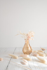 Vintage style of pastel natural colored, beige, and pink foxtail and dried flower in a vase against a white wooden backdrop with space for text. Spring and Autumn inspiration