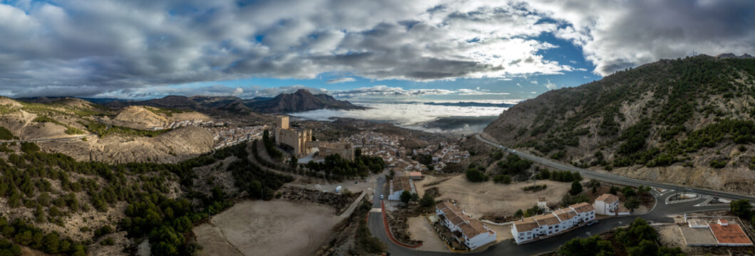 Aerial view of  Velez Blanco castle on a hilltop and town with one or two floor houses whitewashed walls and tiled roofs with dramatic cloudy sky in Andalusia Spain