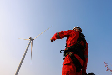 Portrait of engineer with red work uniform with safety hard hat and harness work in wind turbine farm
