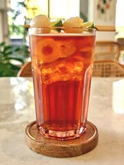 Refreshing lychee tea drink complete with real lychee and ice cubes, served on a table at a cafe during daytime. 